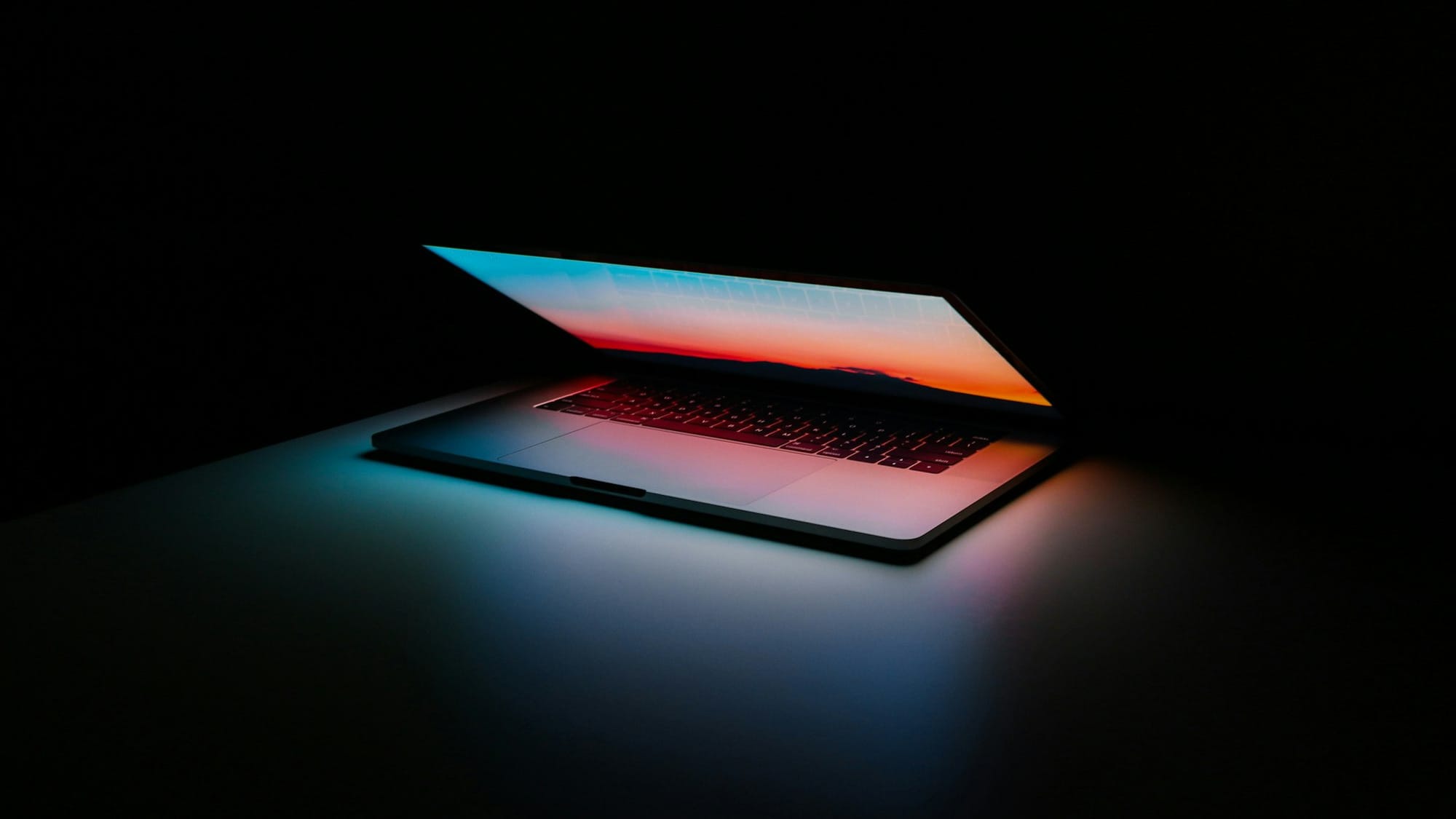 MacBook laptop with the display on and slightly closed in a dark room