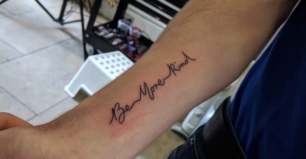 Man's arm with a new tattoo reading Be More Kind