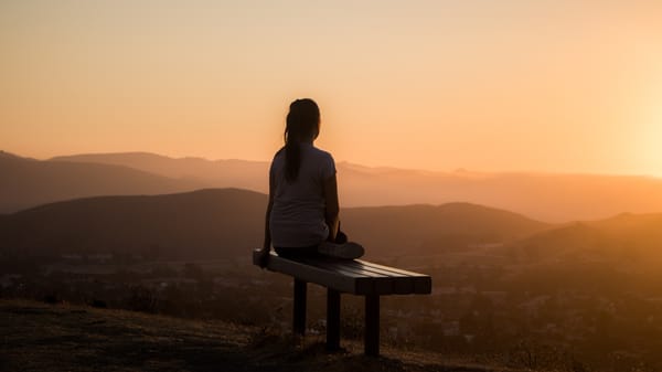 Woman sitting on a bench at the top of a hill at sunset