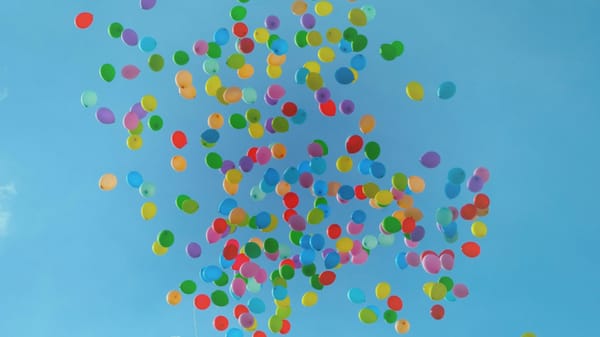Multi-coloured balloons rising up into the air against a bright blue sunny sky